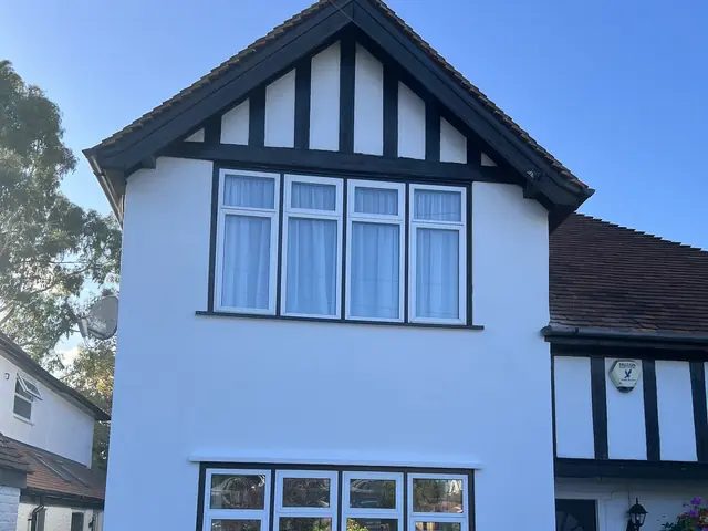 Front of a house with freshly painted white render and black and white timbers on the gable