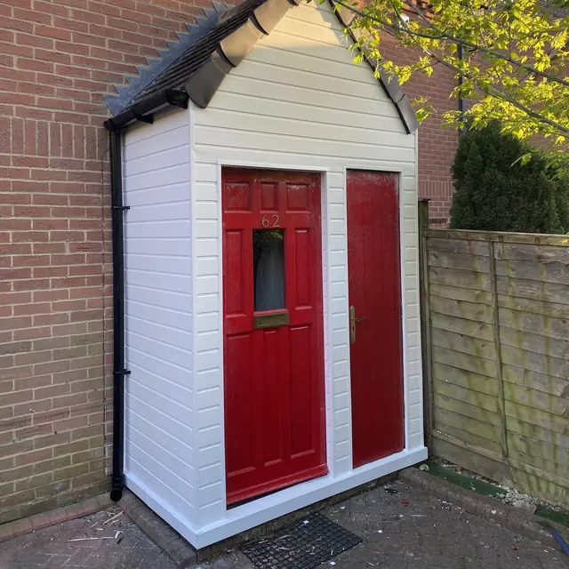 Small porch store clad in new white uPVC cladding, with two red doors