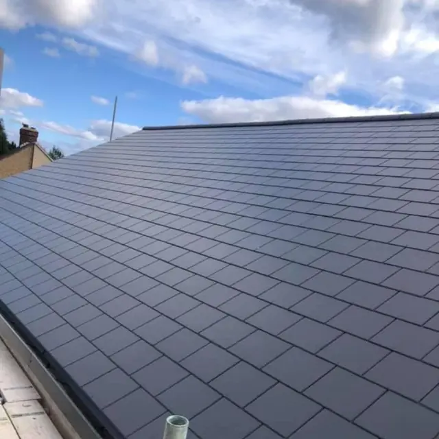 Newly finished roof of dark grey slate-effect tiles under a blue sky