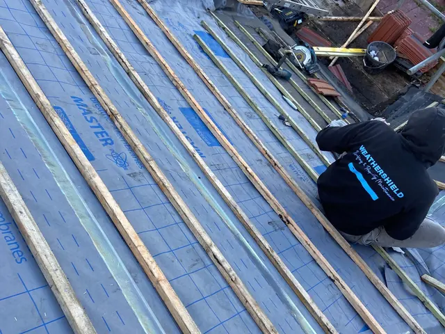 Roofer in a Weathershield hoodie fixing battens over new membrane on a pitched roof